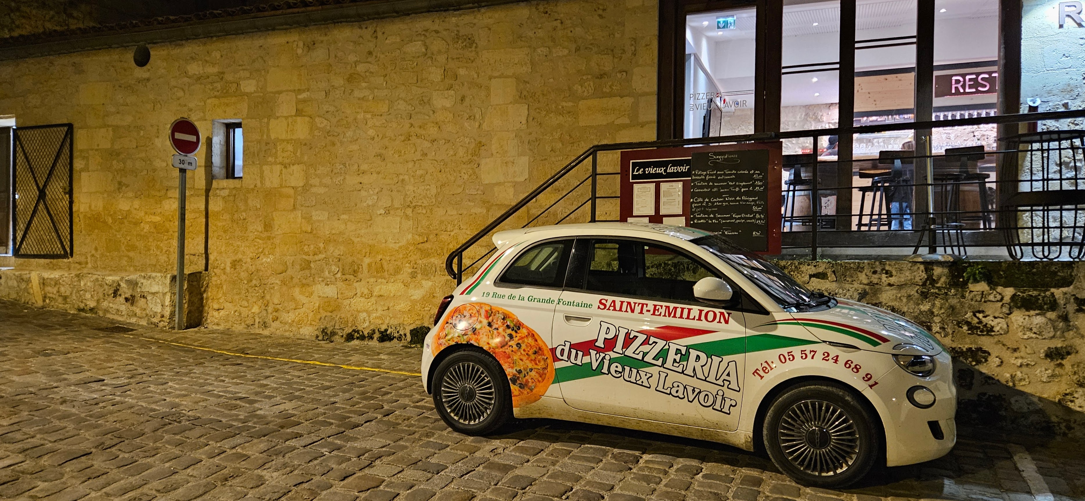 Pizza delivery car on cobblestone street in front of restaurant